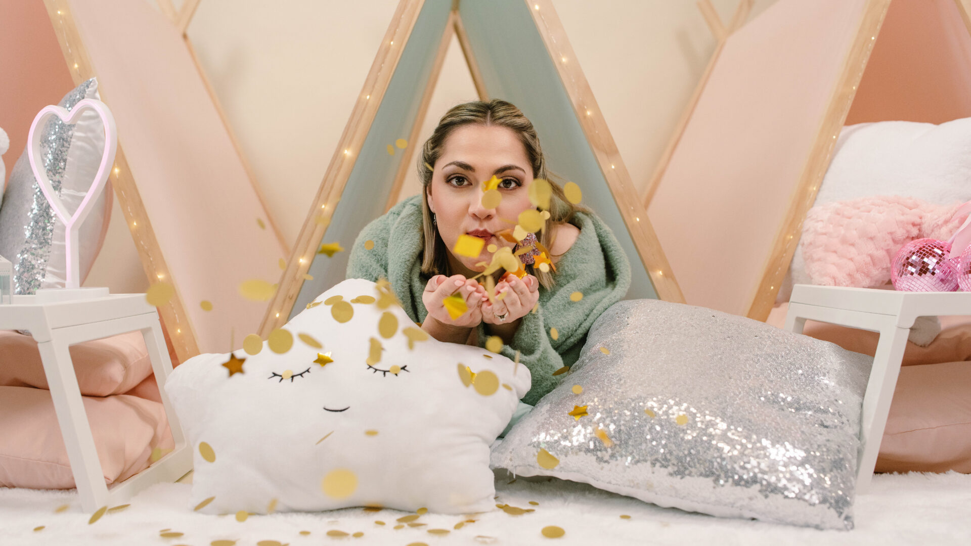 Woman blowing gold confetti in cozy setting.