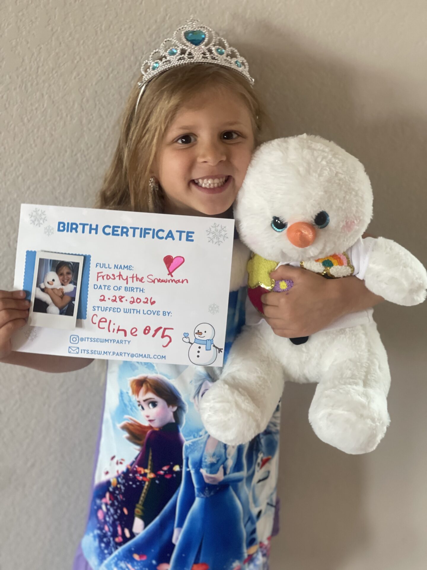 Little girl wearing a crown and holding a teddy bear, with a birthday certificate in her hands