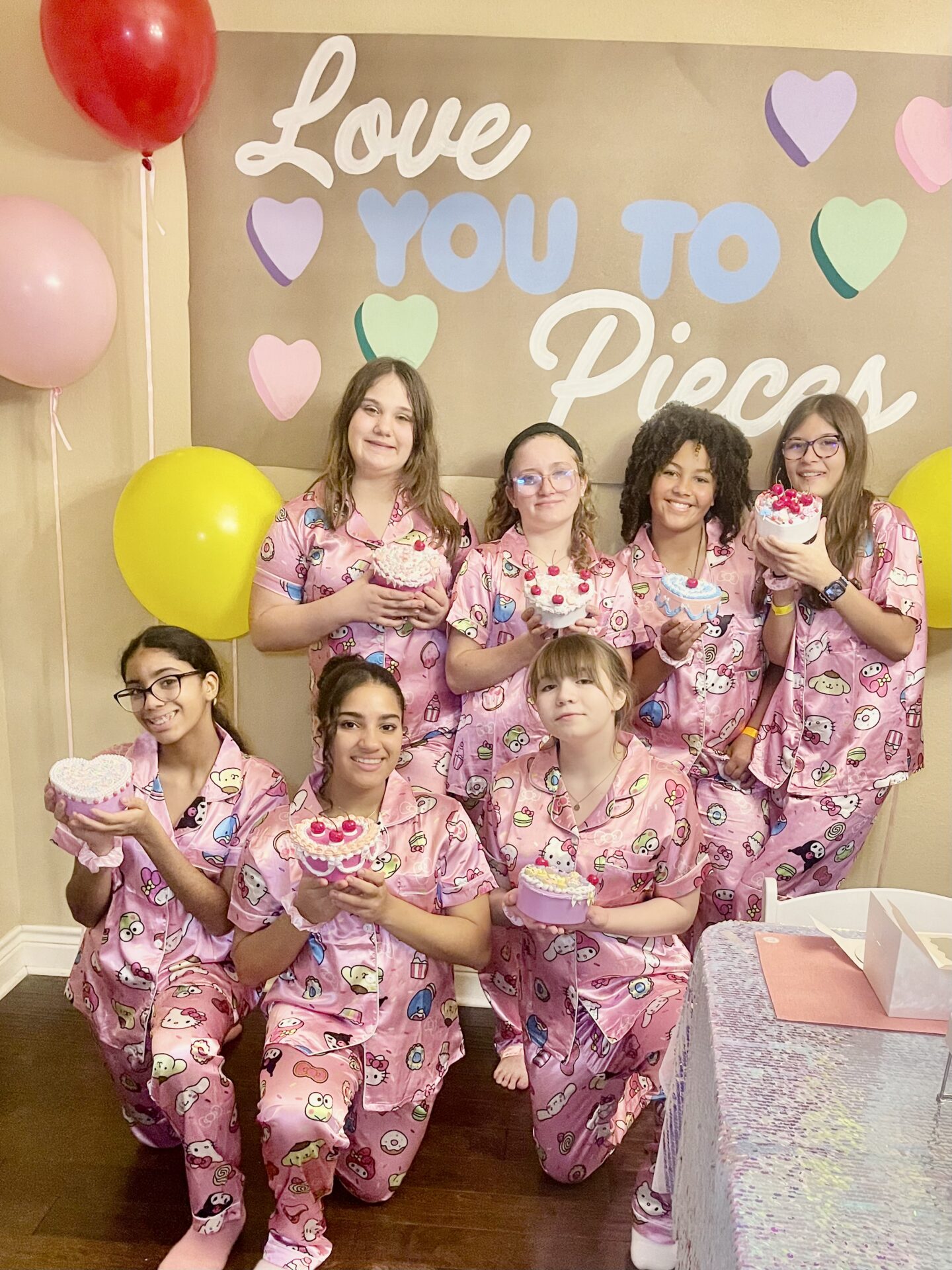Group of women in pink pajamas posing for a photo with cupcakes in their hands
