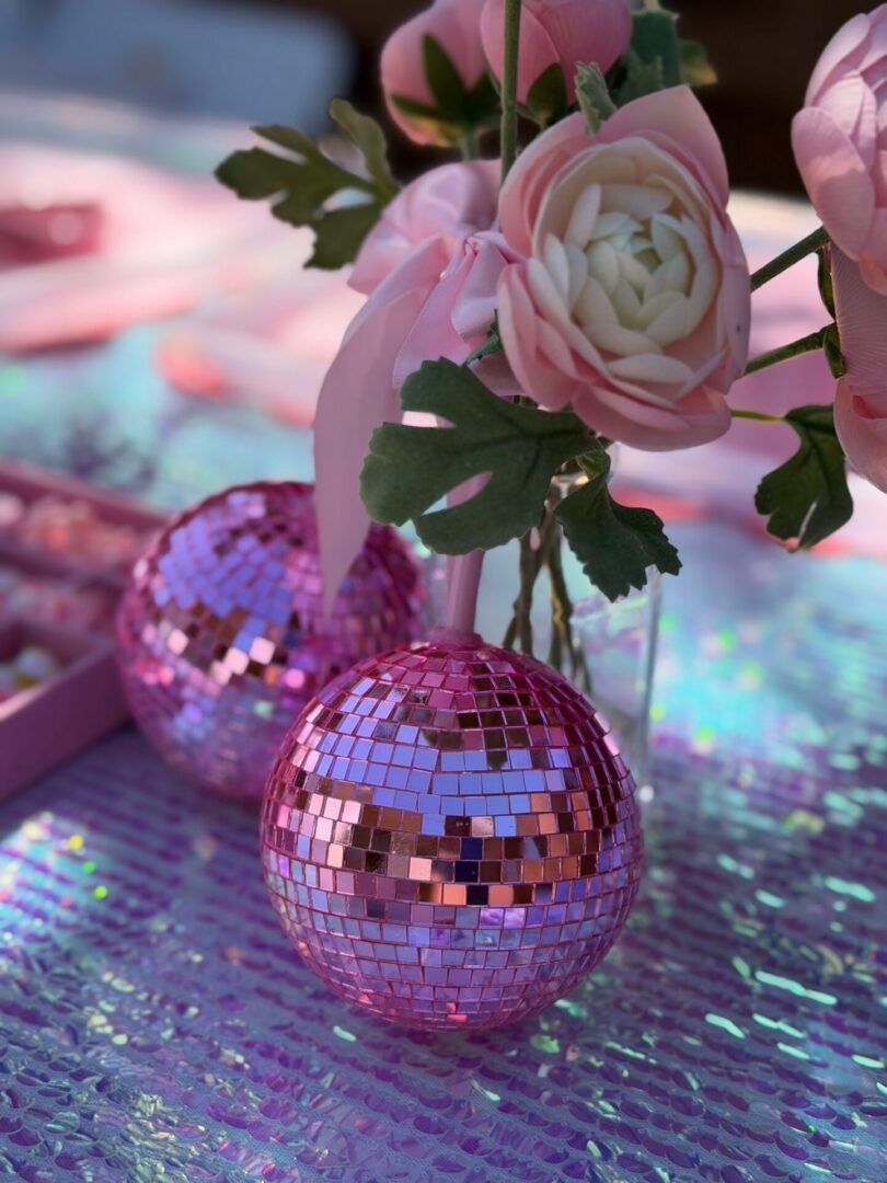 Table topped with pink flowers and two pink disco balls, creating a festive atmosphere perfect for a birthday party