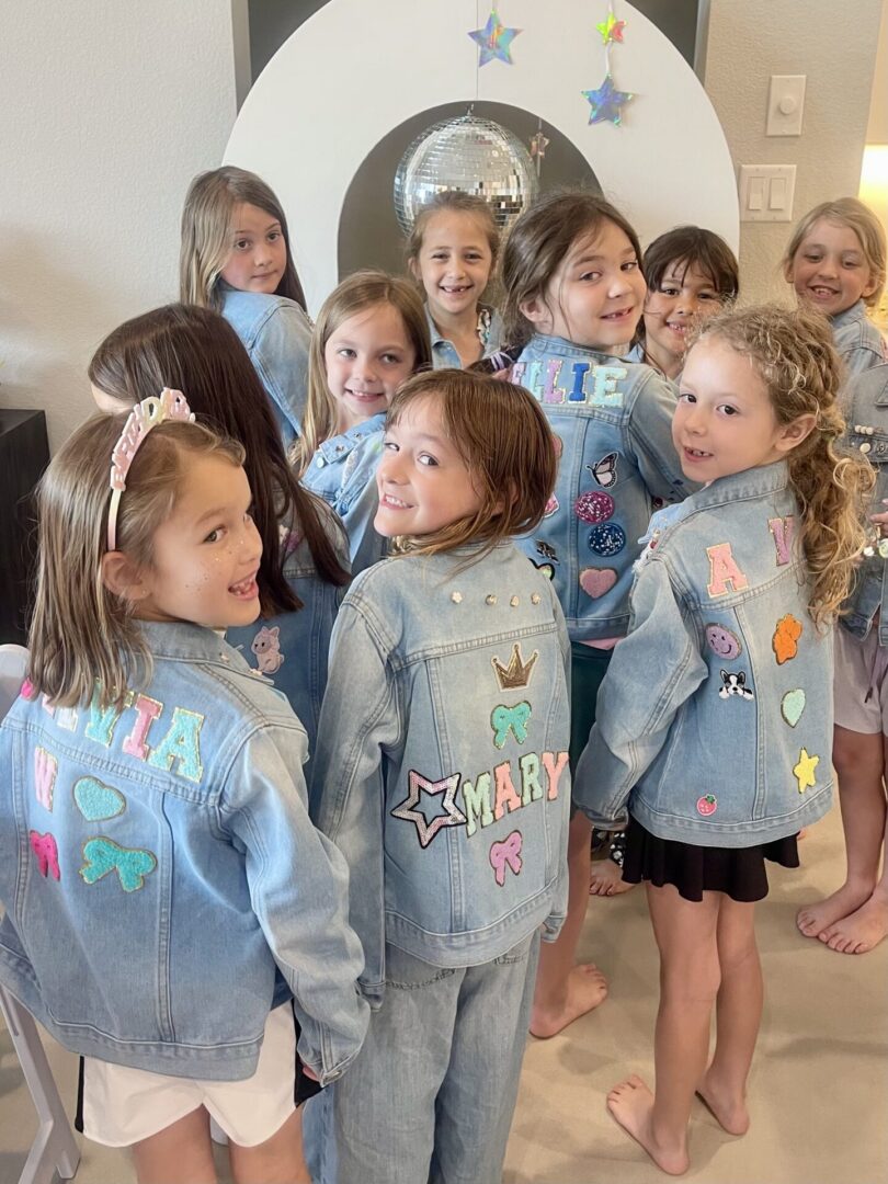 Girls wearing decorated denim jackets, smiling together.