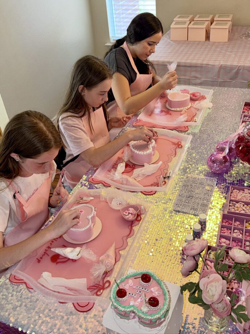 Three girls decorating small pink cakes.
