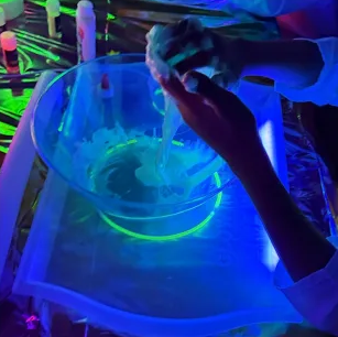 Hands mixing glowing slime under UV light.
