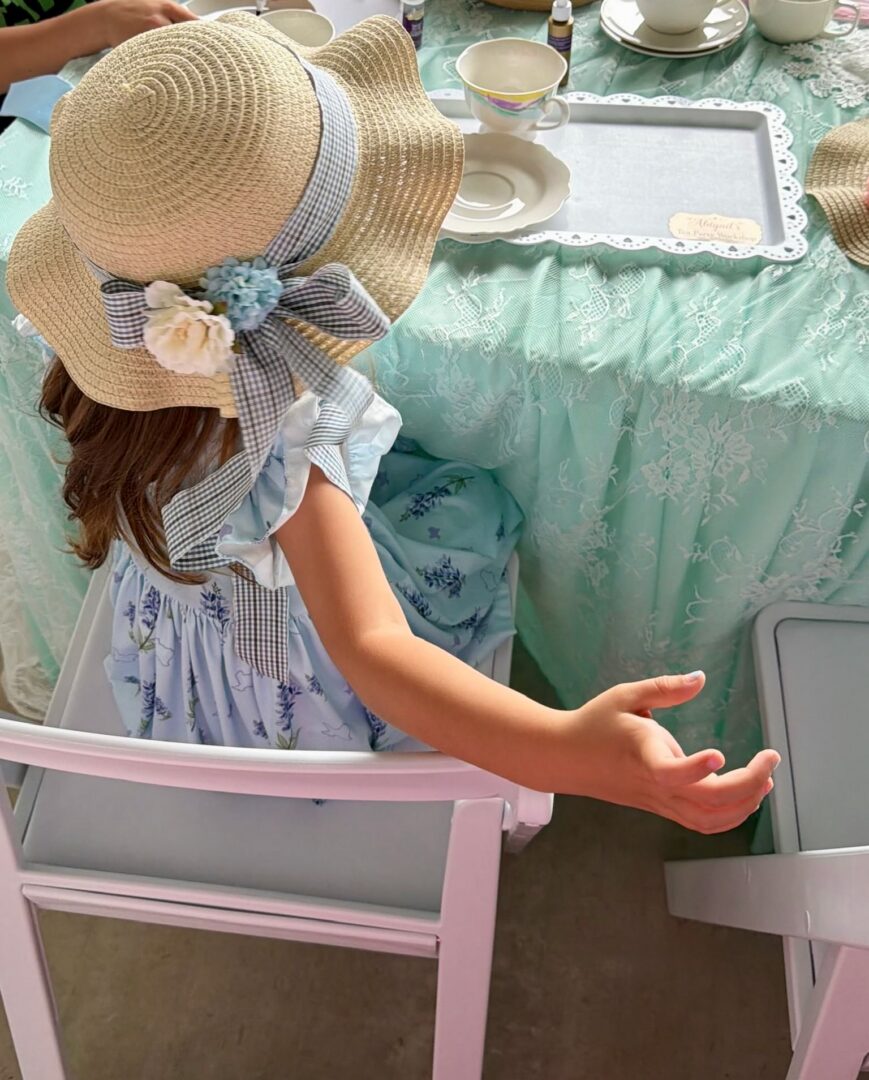 Child in sunhat at tea party table.