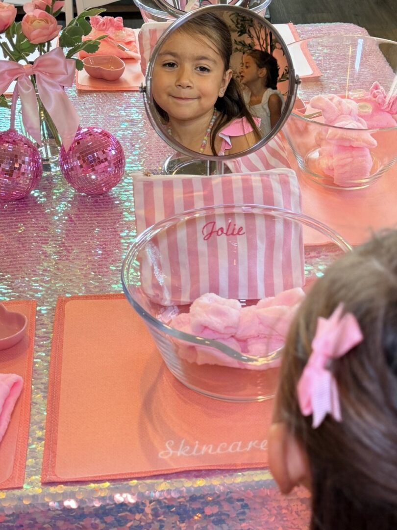 Girl reflected in mirror at pink-themed party.