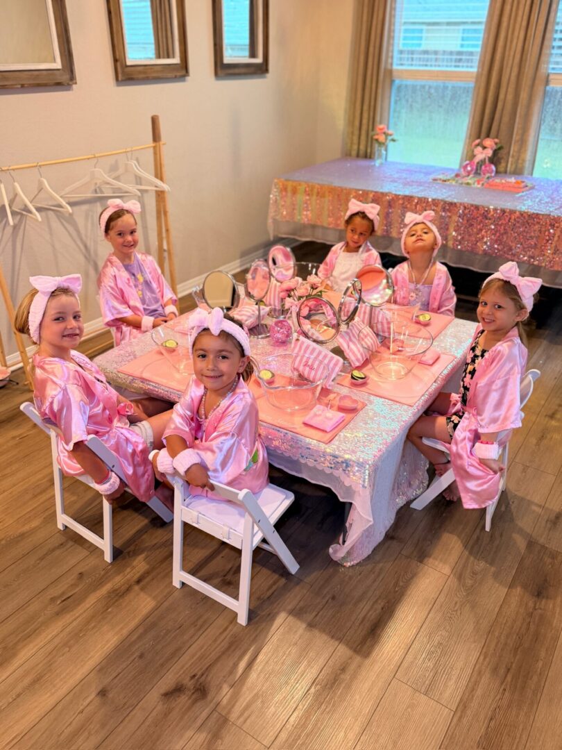 Children in pink robes at party table.