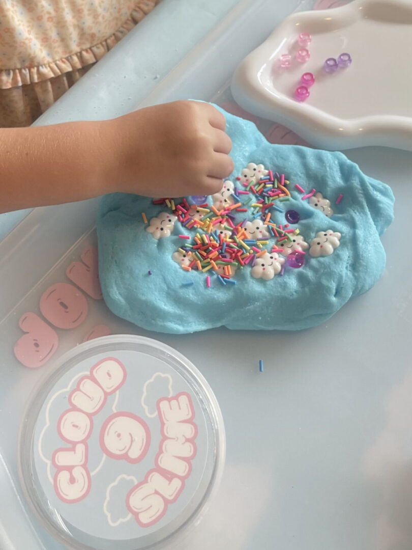 Child decorating blue slime with sprinkles.