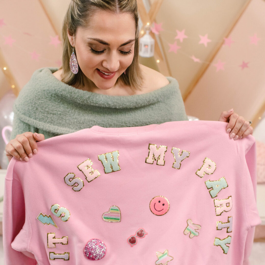 Woman holding pink decorated sweater, smiling.