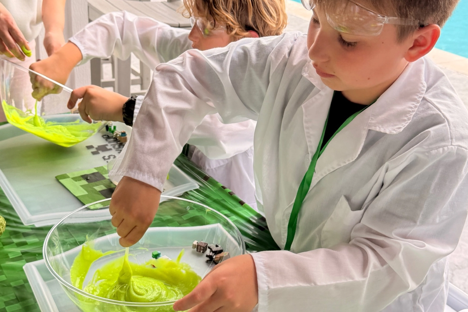 Children making green slime in lab coats.