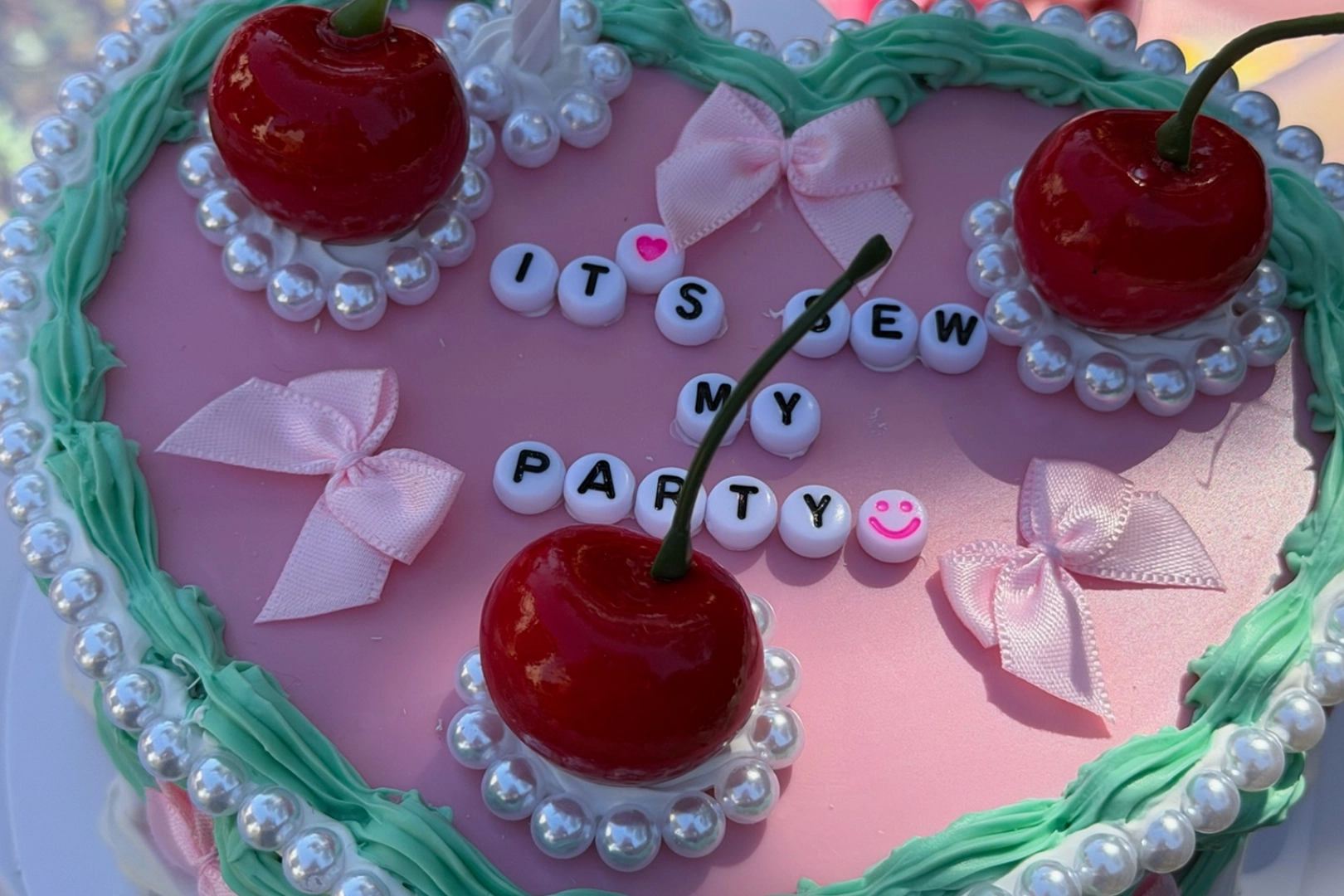 Pink cake with cherries and decorative text.