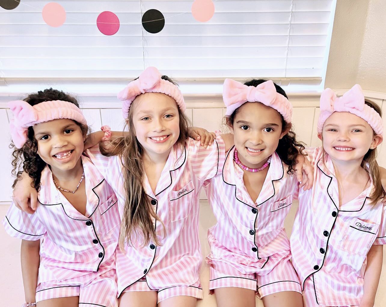 Four girls in matching pink pajamas smiling.