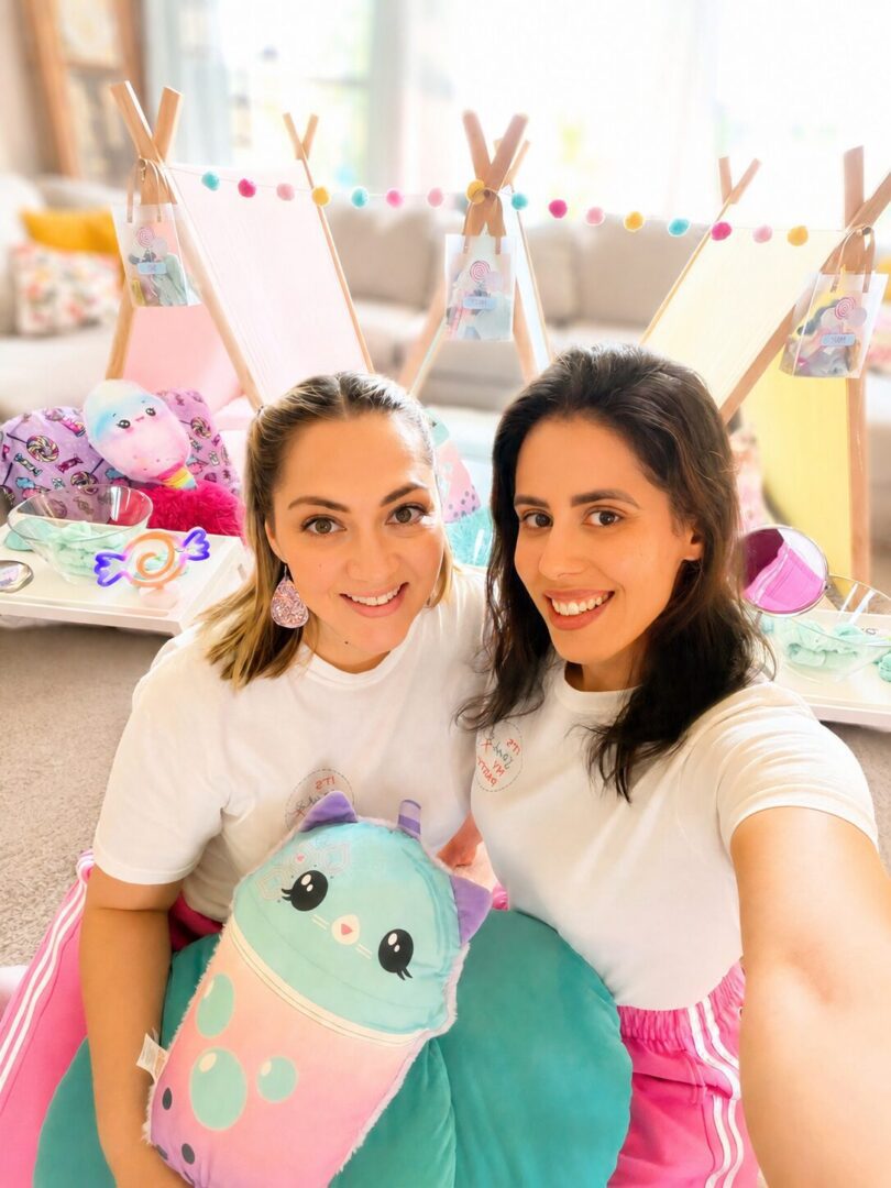 Two women sitting on the floor in front of a teepee, both wearing white t-shirts